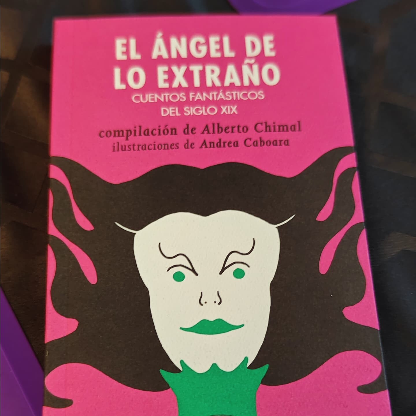 Portada de la antología "El Ángel de lo Extraño" (UNAM, 2024). El libro está inclinado y puesto sobre un mantel negro.